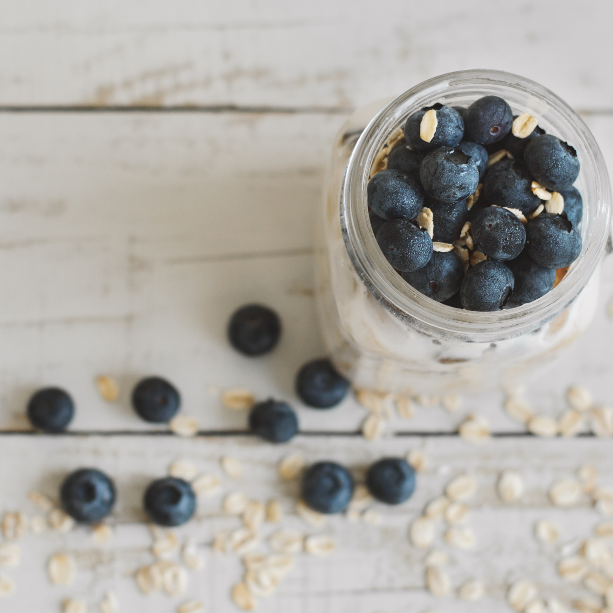 A mason jar with blurberry oats. Around the jar are scattered blueberries.