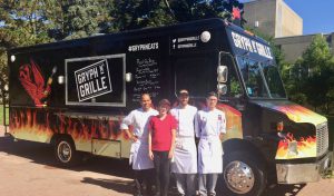 An image of the gryph and grille food truck with chefs standing infront of it.